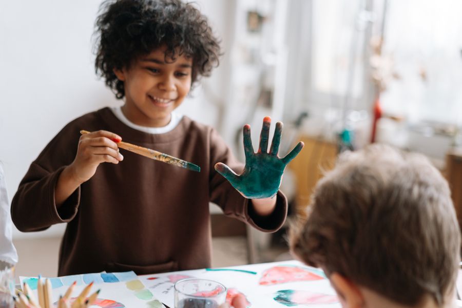 A smiling child painting with paint-covered hands in the art studio
