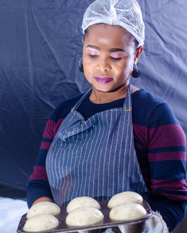 Indian woman baker in a hair net holding a tray of buns