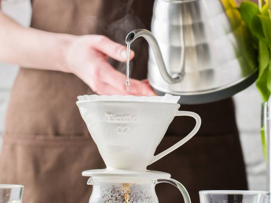 Barista pouring hot water from a kettle into a ceramic pour-over dripper