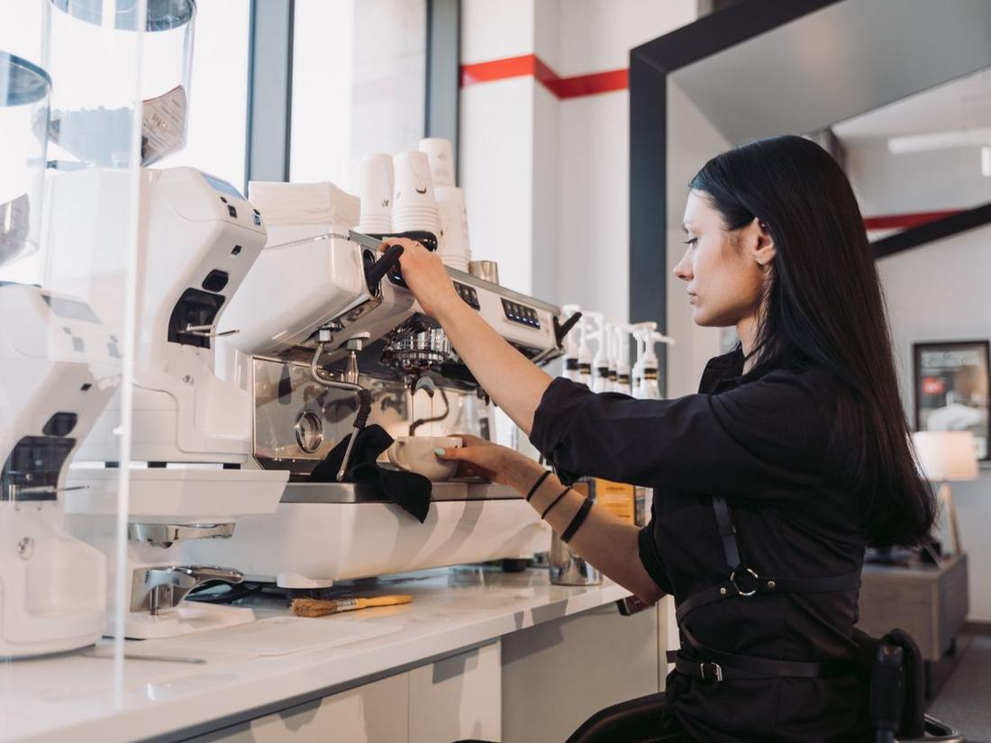 Indian woman barista in an apron working at an espresso machine