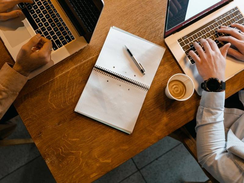 Hands typing on a laptop beside a coffee cup and notebook