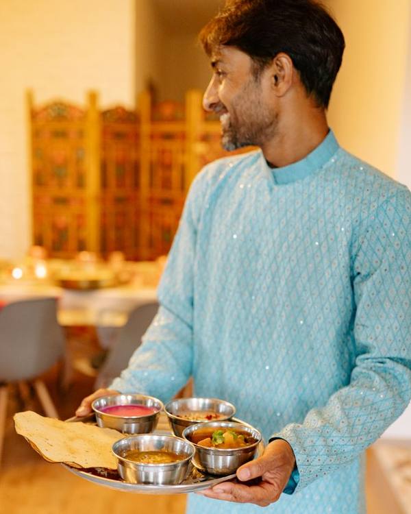 Indian man in a blue kurta holding plates of food