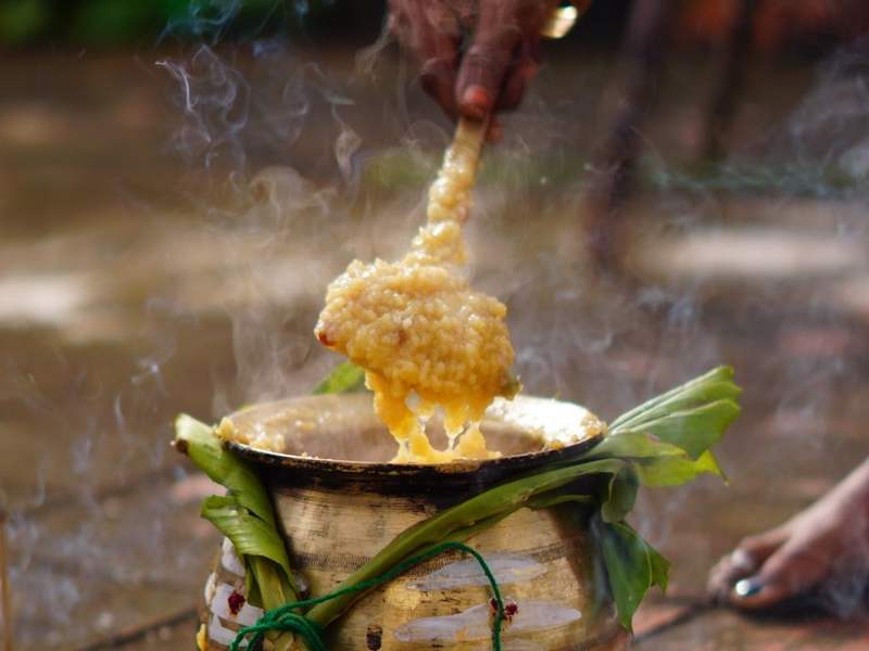 Hand ladling payasam from a brass uruli onto a banana leaf