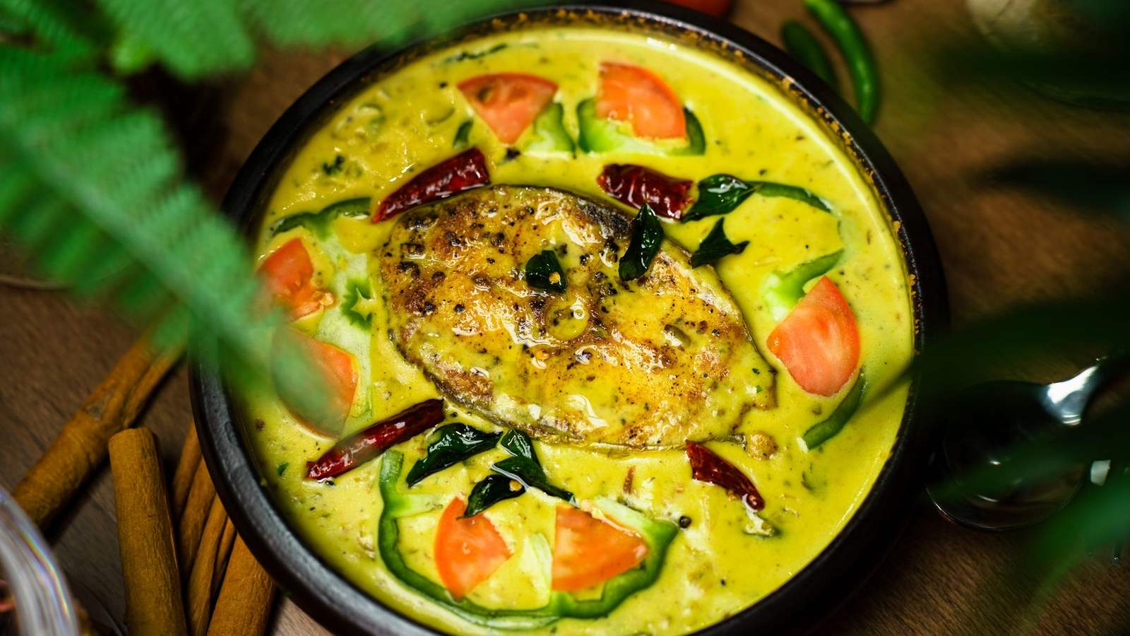 Kerala fish moilee in a black pan with tomato, curry leaves and coconut, on a dark wooden table