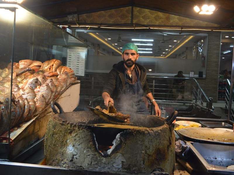 Cook grilling fish over charcoal at an open counter