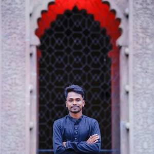 Indian man in a dark blue kurta standing in a red-lit arched doorway
