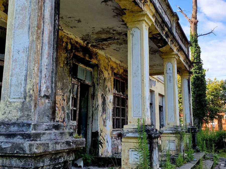 Weathered heritage mansion with tall stone pillars and creepers
