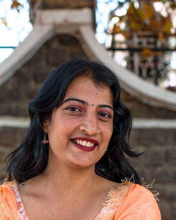 Smiling Indian woman in an orange kurta in front of a heritage building