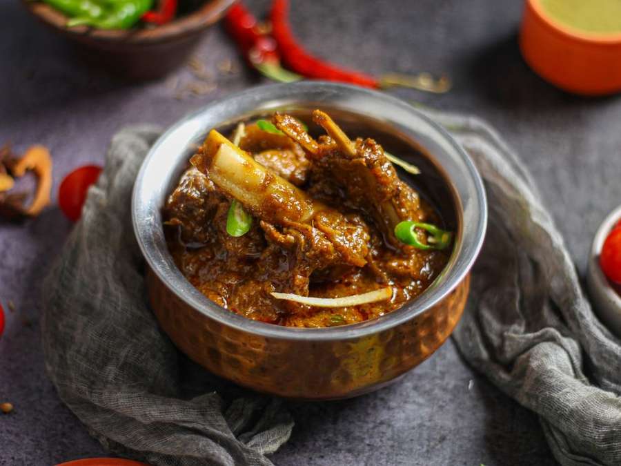 Mutton curry in a copper vessel on a dark grey cloth