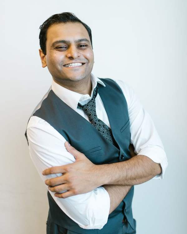 Smiling Indian man in a grey waistcoat with arms crossed