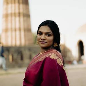 Indian woman in a maroon saree smiling in front of a heritage tower