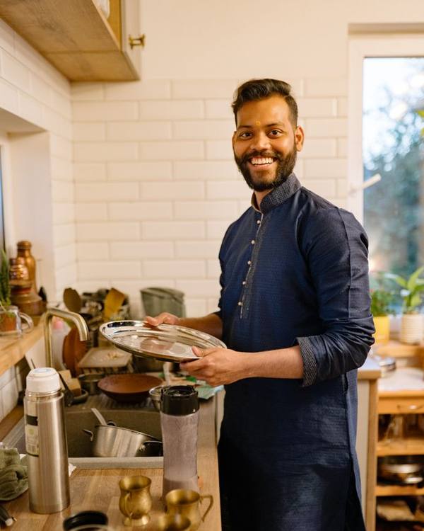 Smiling Indian man in a dark kurta holding a plate in a café kitchen
