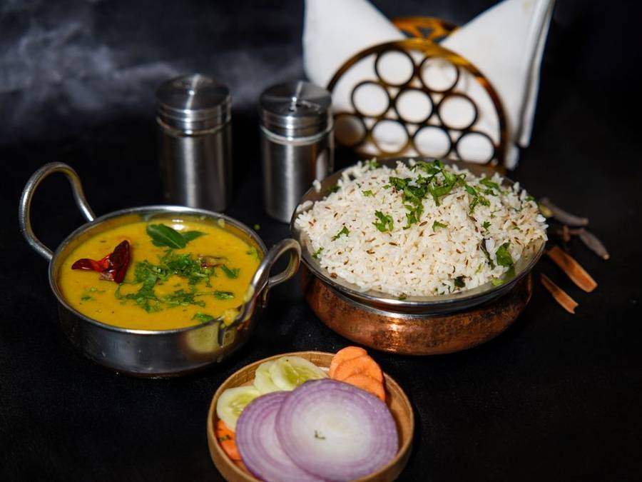 Dal and rice served in copper vessels with onions and lime
