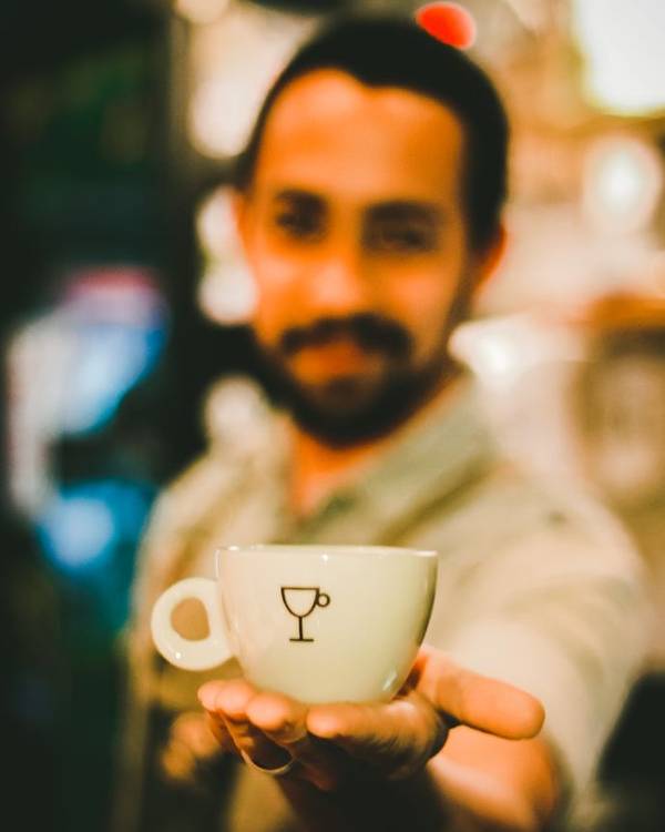Indian man in a café holding out a cup of coffee