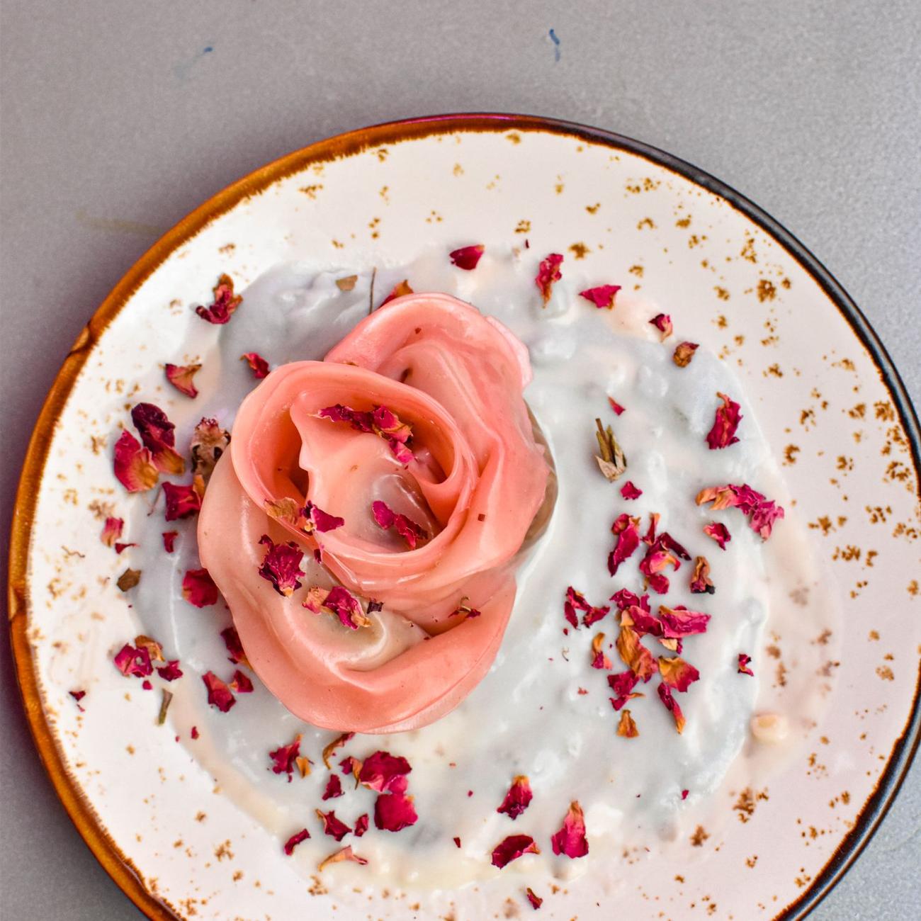 Rasmalai plated as a rose with dried petals and pistachio on a round blush plate