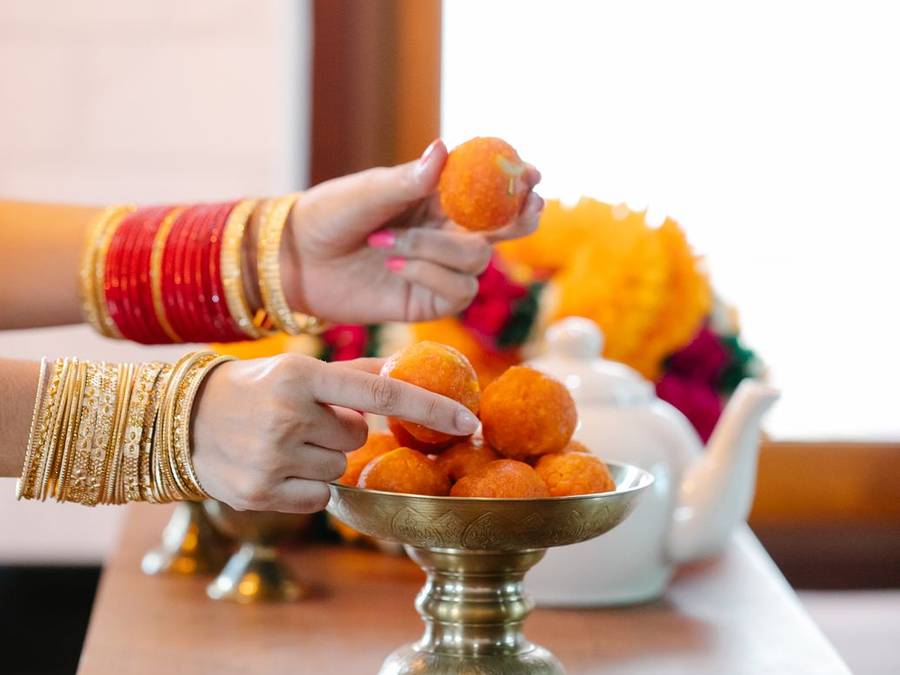 Hands reaching for Indian sweets on brass stands decorated with flowers