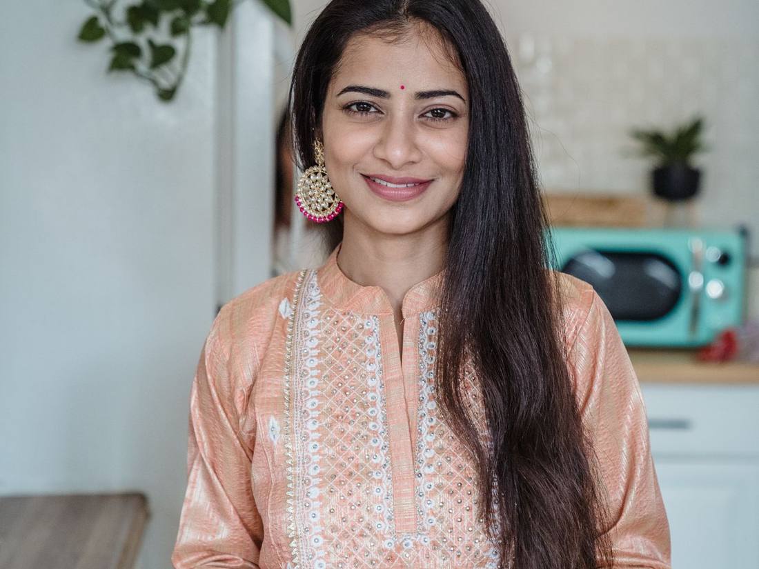 Smiling Indian woman in an embroidered peach kurta in the café kitchen