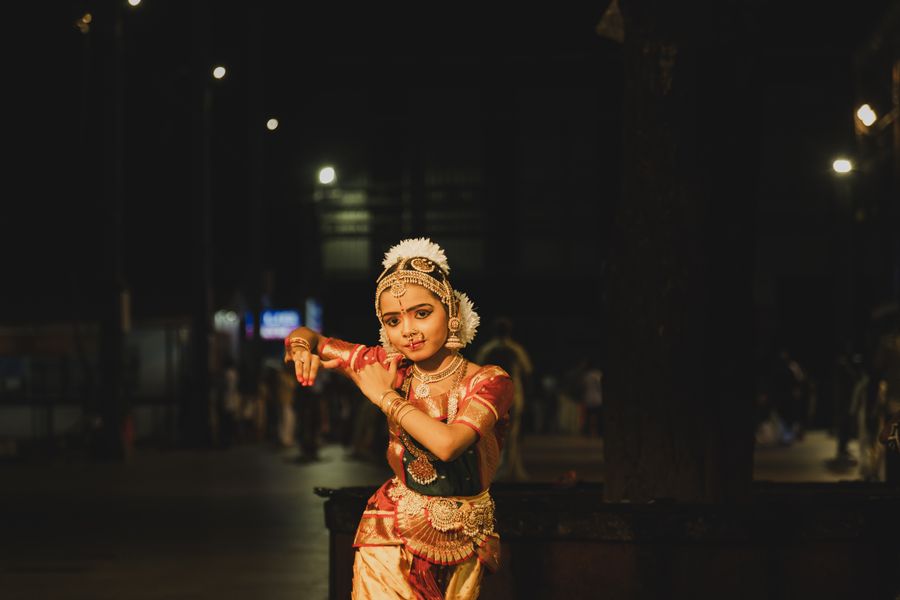 A Bharatanatyam dancer posing in traditional costume under night lights