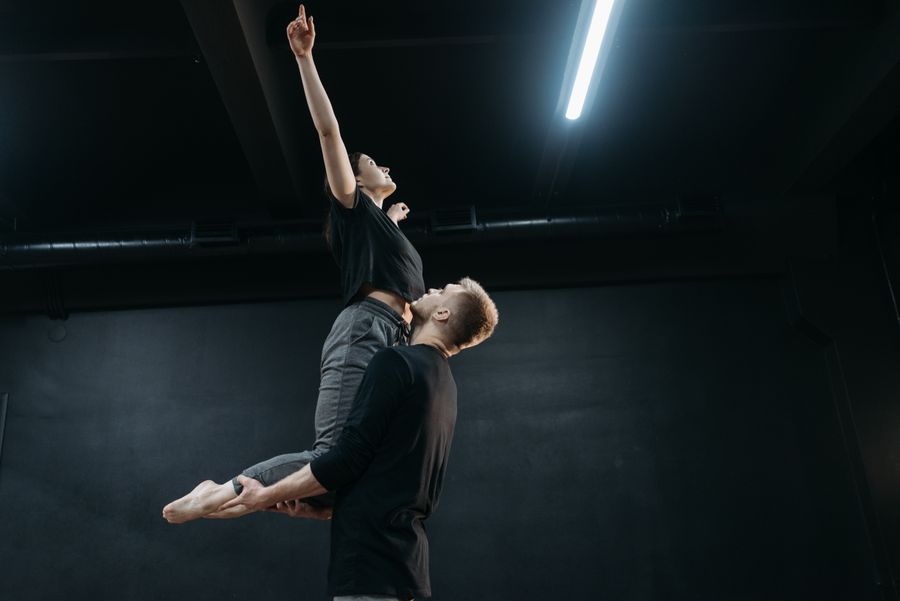 Two contemporary dancers performing an expressive lift in a dark studio