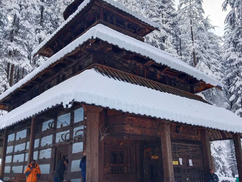 Two-storey timber Himachali house with a slate roof under fresh snow