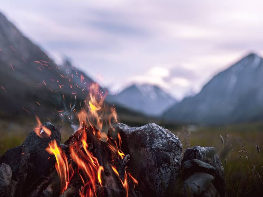 Campfire burning at dusk with mountain ridges behind