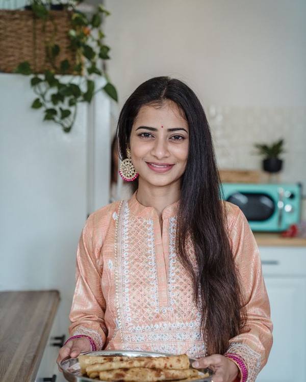 Indian woman in a peach kurta holding a tray of freshly baked food