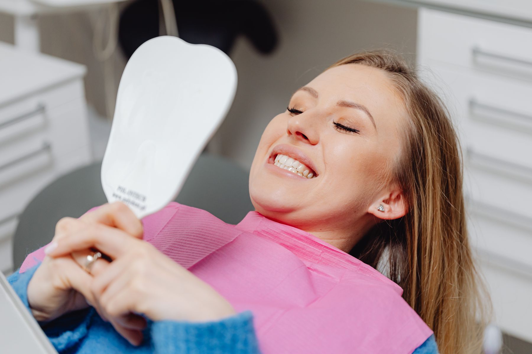 A delighted patient admiring her whitened smile in a hand mirror