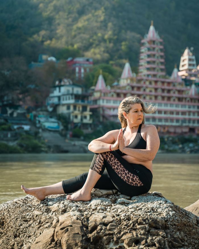 Dr. Kavita Rawal practising yoga beside the Ganga with a temple in the background
