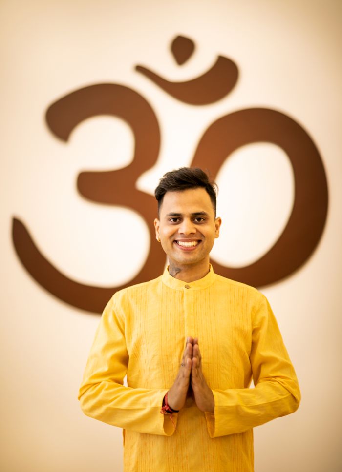 Swami Prakash Giri smiling in yellow robes before an Om symbol