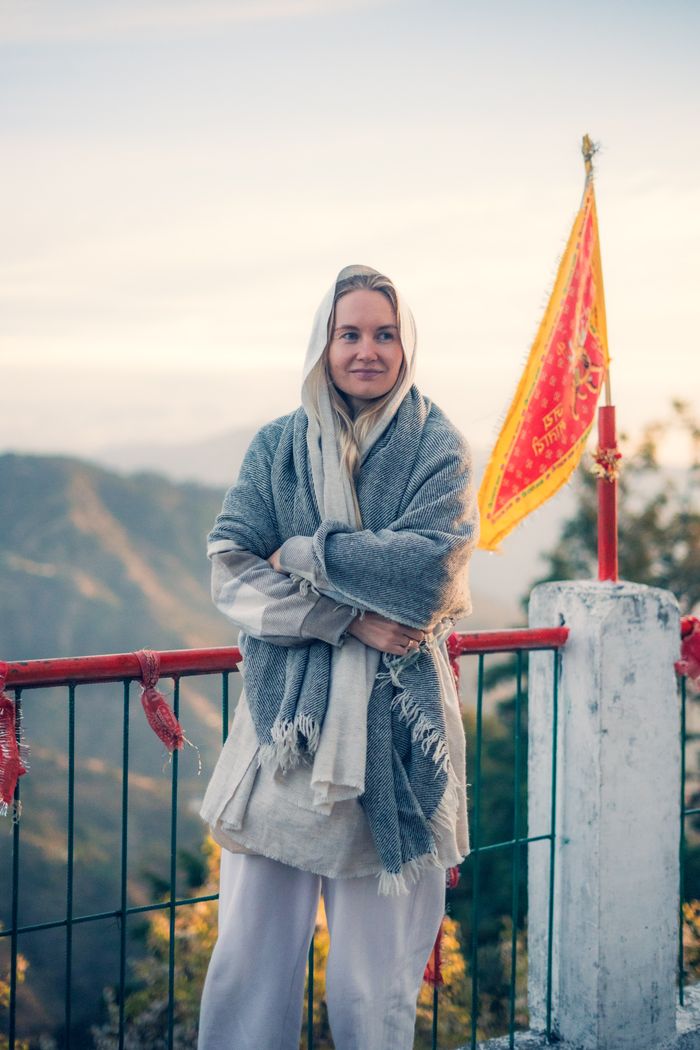 Ananya Chauhan wrapped in a shawl on the ashram balcony, mountains behind her