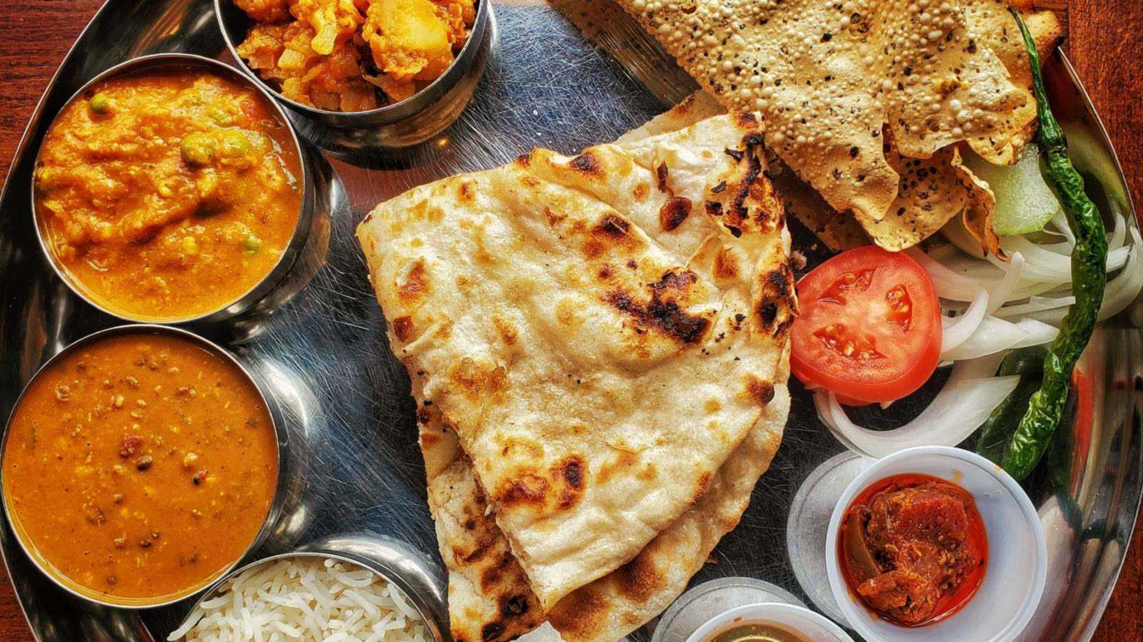Overhead view of a Rajasthani thali with dal, baati, churma, gatte ki sabzi and rotis on a brass platter