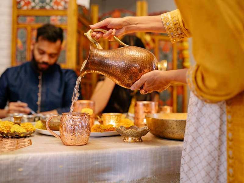 Water poured from a brass jug at a traditional Indian dining table