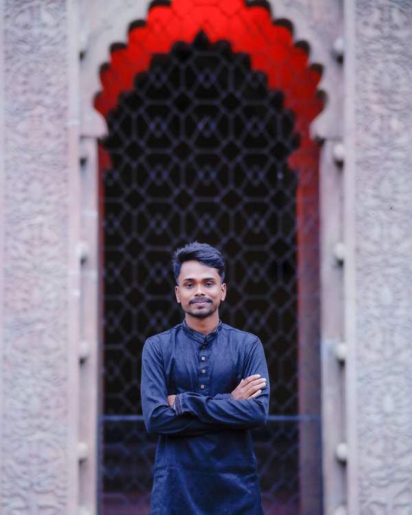 Indian man in a blue kurta standing in a red-painted jharokha archway