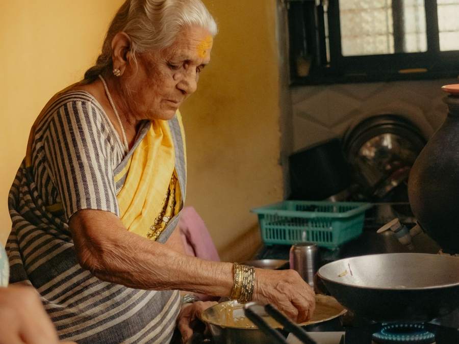 Elderly Goan woman cooking in a sunlit home kitchen