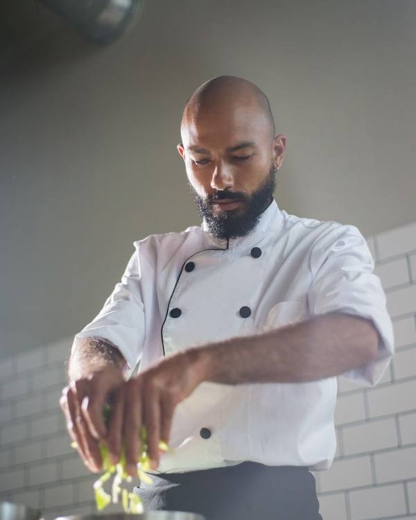 Indian chef in whites whisking sauce in a steel bowl