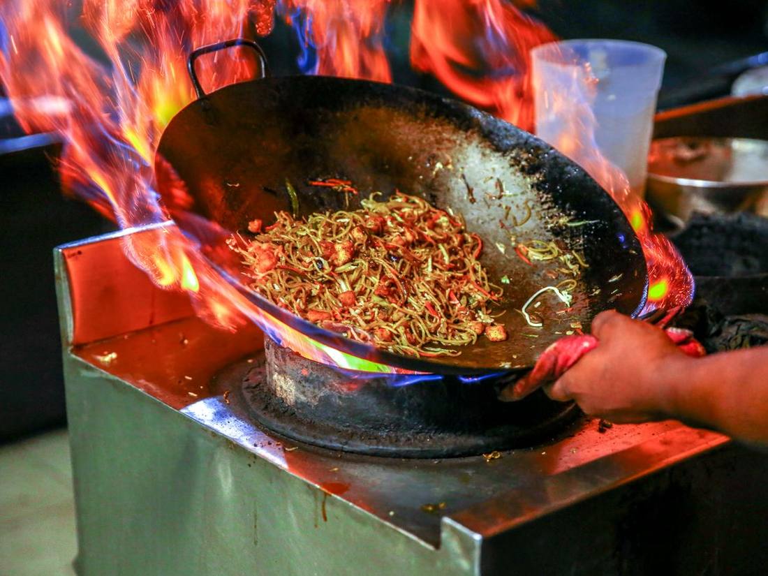 Flames leaping from a wok on a red-lit burner in the Tangra Wok kitchen