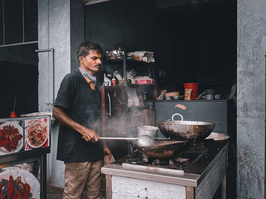 Indian cook working a large wok on an outdoor burner in Tangra