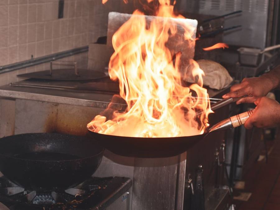 Chef tossing food in a flaming wok at an open kitchen counter