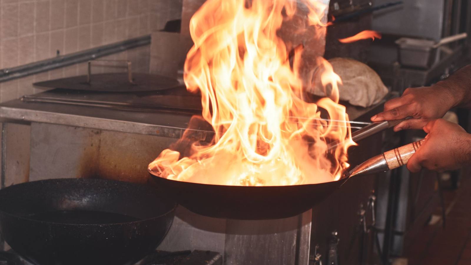 Chef tossing vegetables in a flaming wok in a dark restaurant kitchen