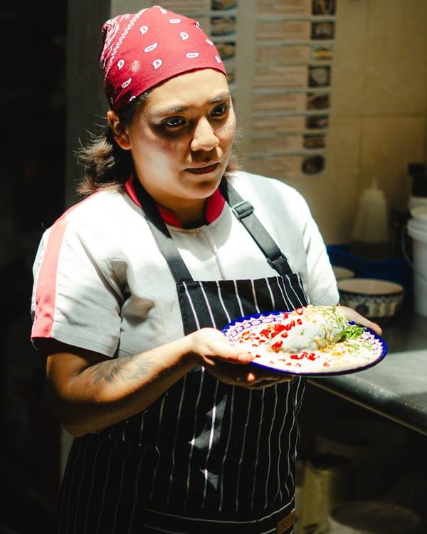 Indian woman chef in a bandana holding a plated dish in a kitchen