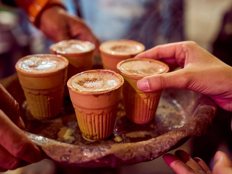 Hands lifting kulhads of chai from a tray