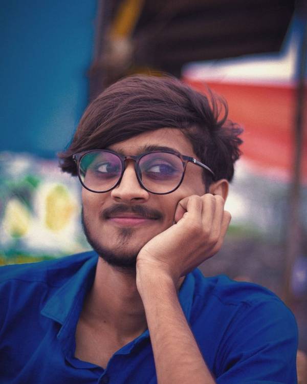 Young Indian man in glasses smiling against a blue background