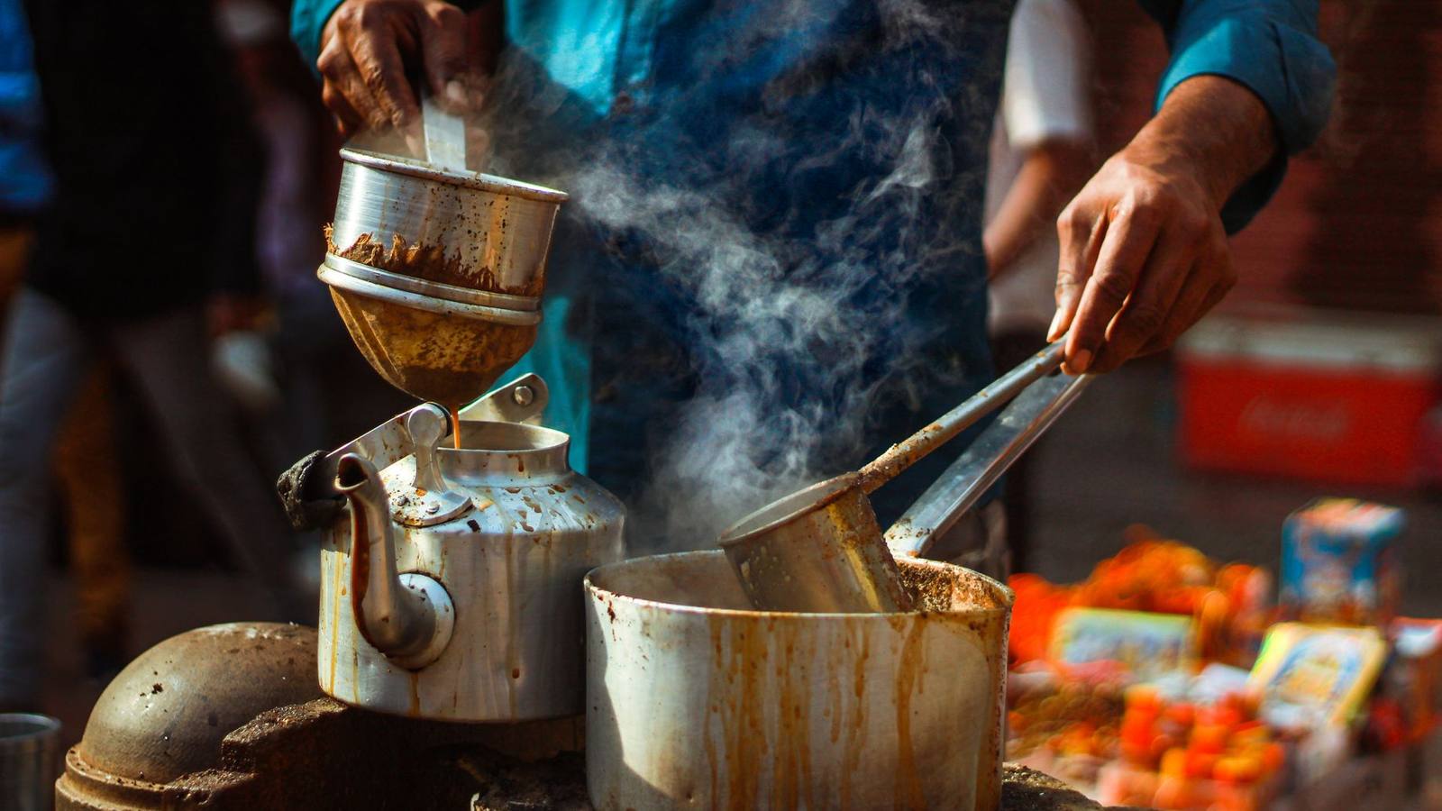 Steaming chai being poured from a kettle into a pan at a Delhi chai stall