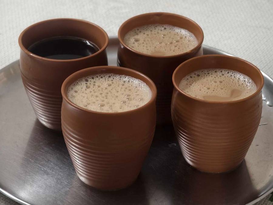 Five clay kulhads of chai on a steel tray