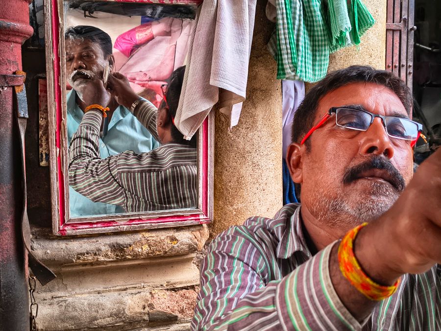 A barber shaving a customer's beard, seen in reflection