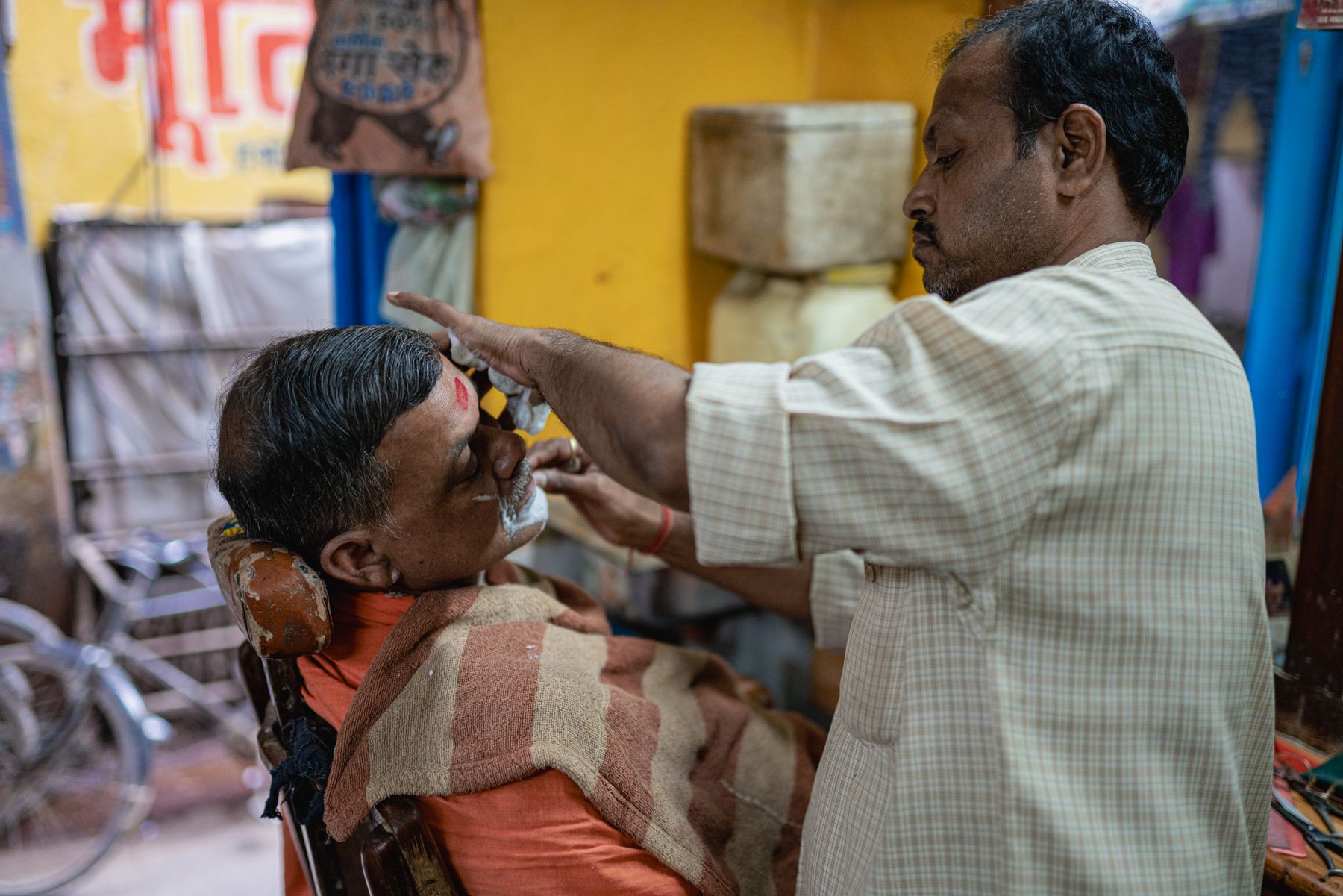 A barber giving a customer a traditional shave in a heritage Indian barbershop