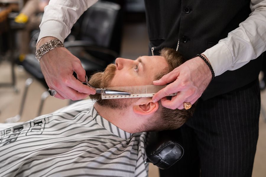 A barber trimming a customer's beard with comb and scissors