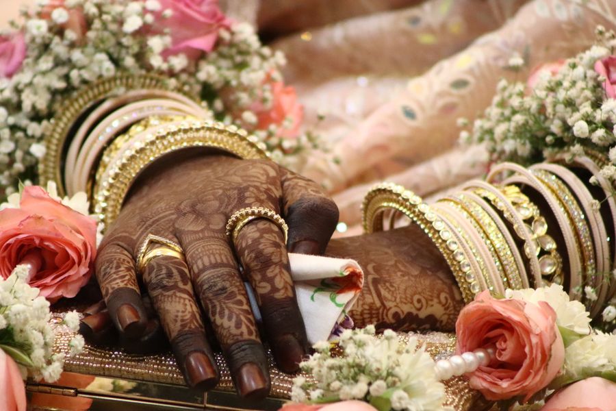 A bride's henna-covered hand with gold jewellery resting among flowers