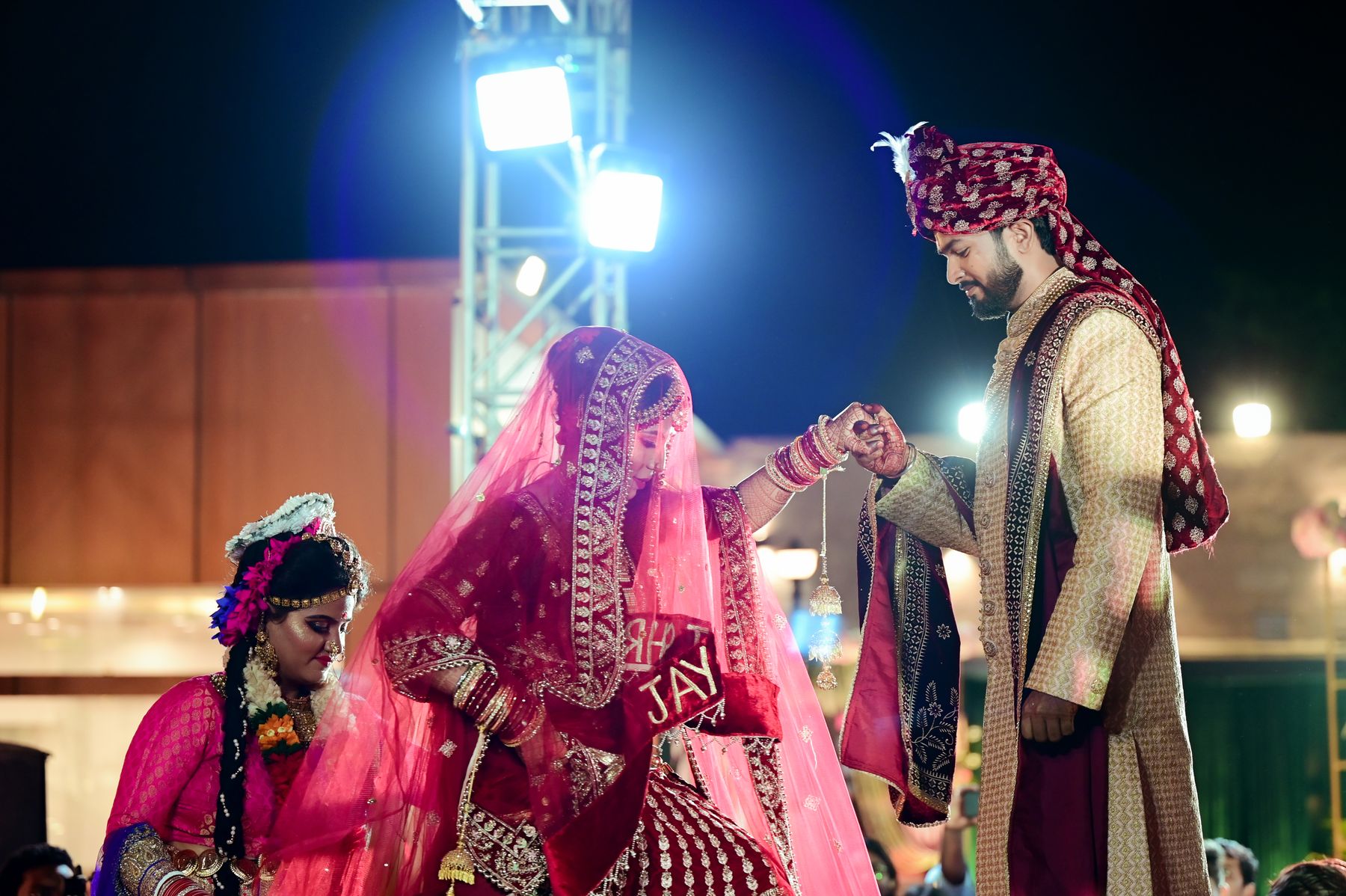 A bride and groom in traditional attire beneath glowing lights at an elegant Indian wedding