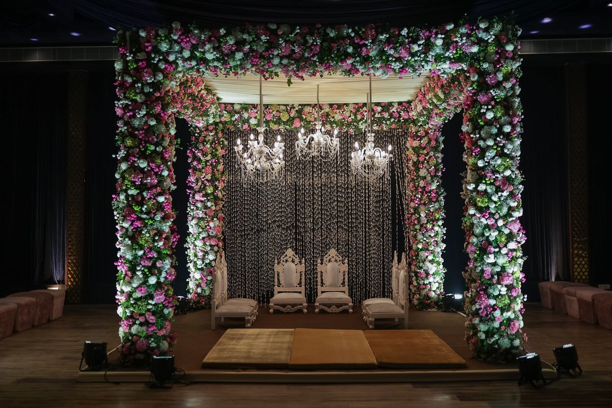 A luxurious floral wedding mandap lit by chandeliers, designed for an indoor ceremony
